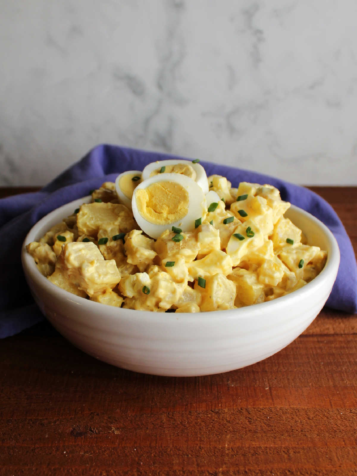 White serving bowl filled with deviled egg potato salad with a yellow mustard dressing and lots of hard boiled eggs.