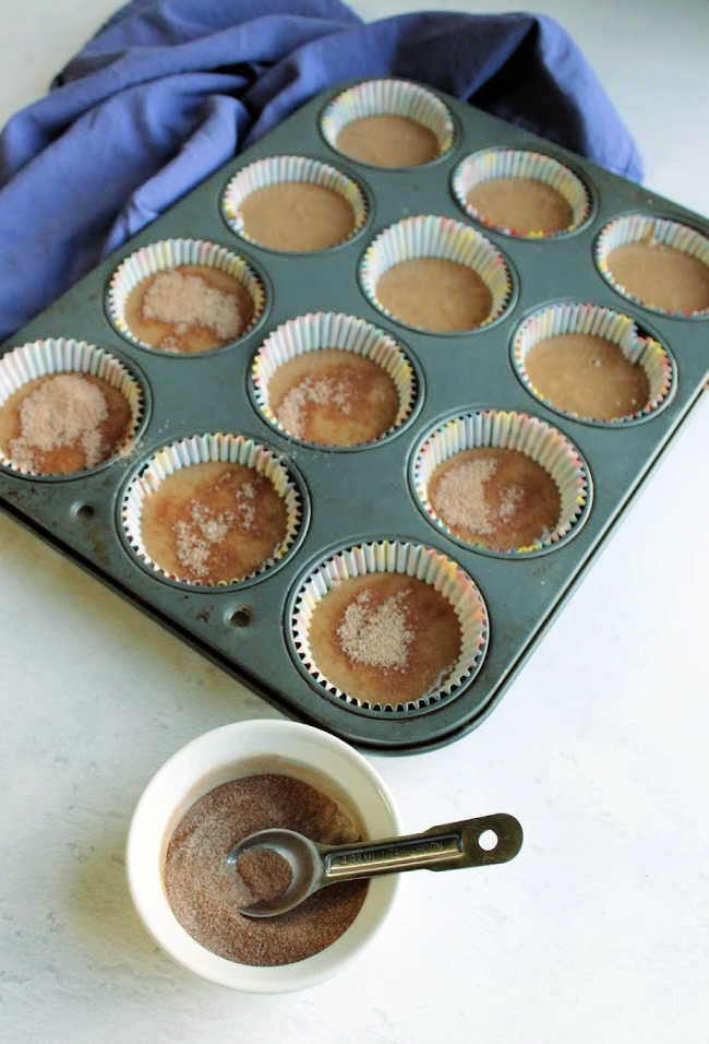 sprinkling cinnamon sugar mixture over muffin batter in tin, ready to bake.