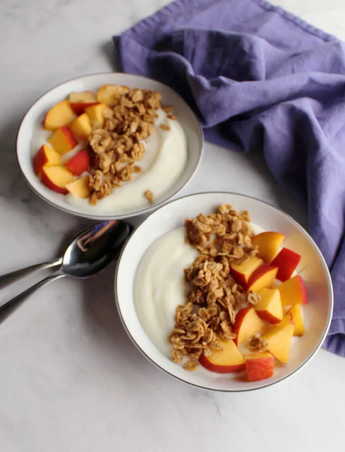 two bowls of yogurt with peach pieces and fresh granola.
