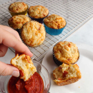 hand dipping muffin into pizza sauce with remaining muffins in background.