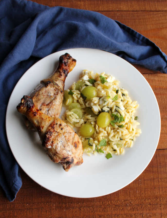 plate of grilled chicken legs and grape orzo salad.