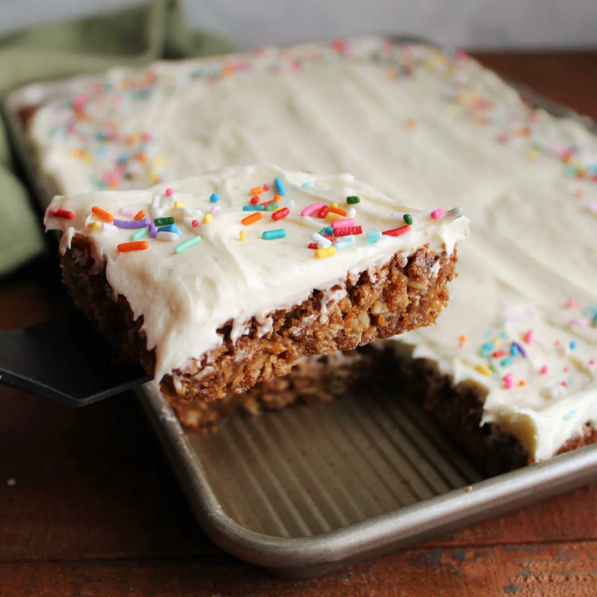 Spatula lifting out first square of oatmeal cream pie bars with chewy molasses and oatmeal cookie layer topped with fluffy white marshmallow fluff buttercream and sprinkles.
