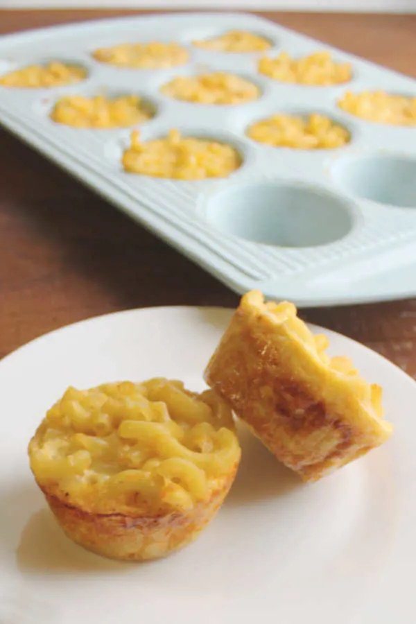 two servings of mac and cheese on plate with cupcake tin filled with more in background