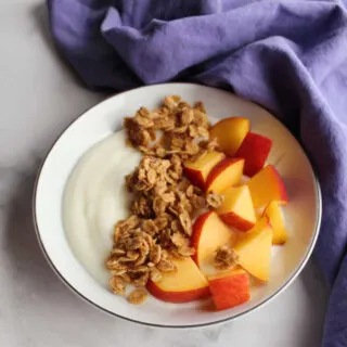 small bowl filled with yogurt, pieces of fresh peach and granola.