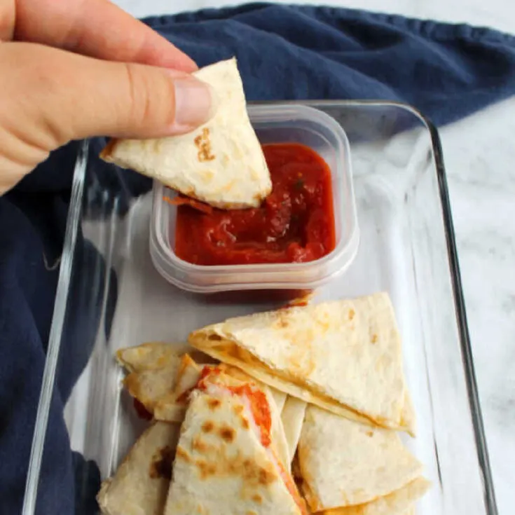 Hand dipping piece of pepperoni quesadilla into pizza sauce.