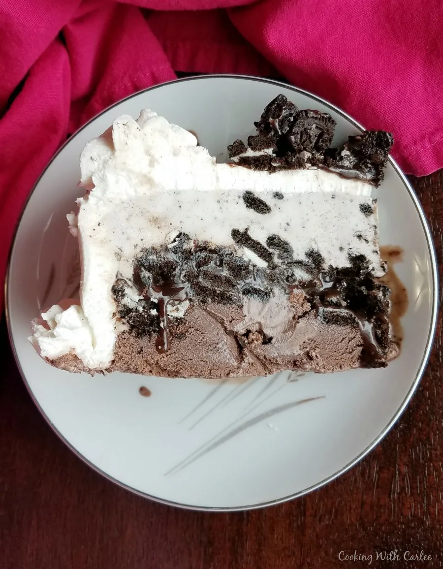 slice of ice cream cake with chocolate ice cream layer, fudge layer, white ice cream layer and cookie topping