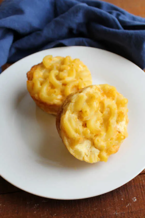 Two macaroni and cheese muffins on a small plate, ready to eat. 