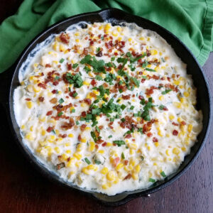cast iron pan filled with creamy corn dip and topped with bacon and fresh herbs.