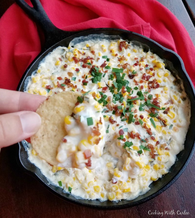 hand holding tortilla chip with creamy spicy corn dip on it.
