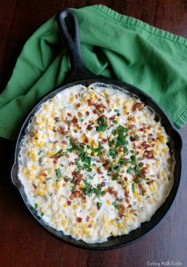 cast iron skillet filled with creamy corn dip topped with bacon, cilantro and chives.