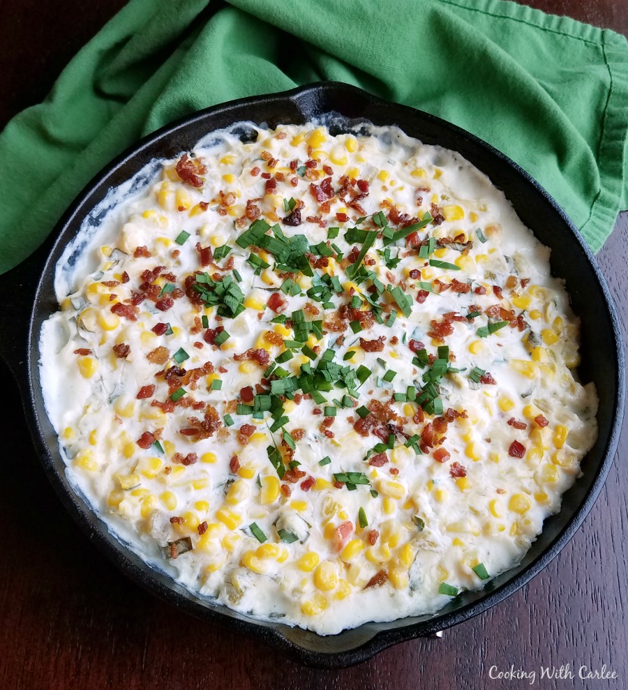 cast iron pan filled with creamy corn dip and topped with bacon and fresh herbs