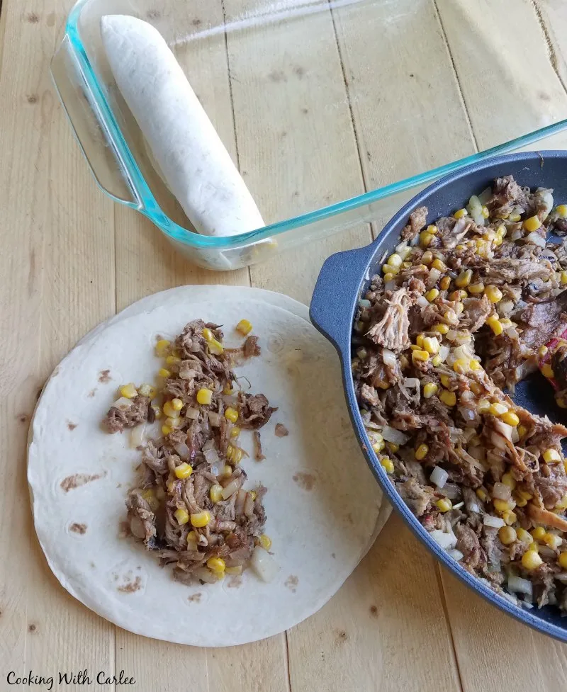 skillet filled for bbq pulled pork and corn mixture being scooped onto tortillas and rolled into enchiladas