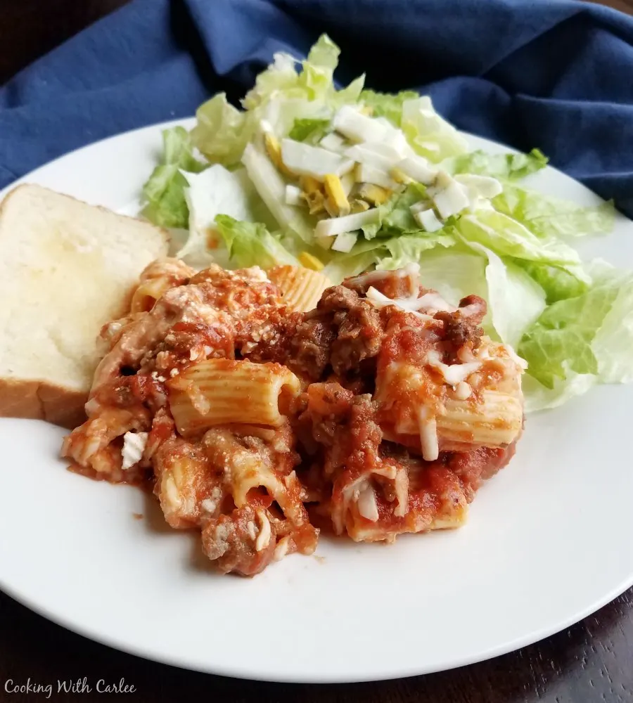dinner plate with helping of baked ziti made with rigatoni, salad and garlic bread.
