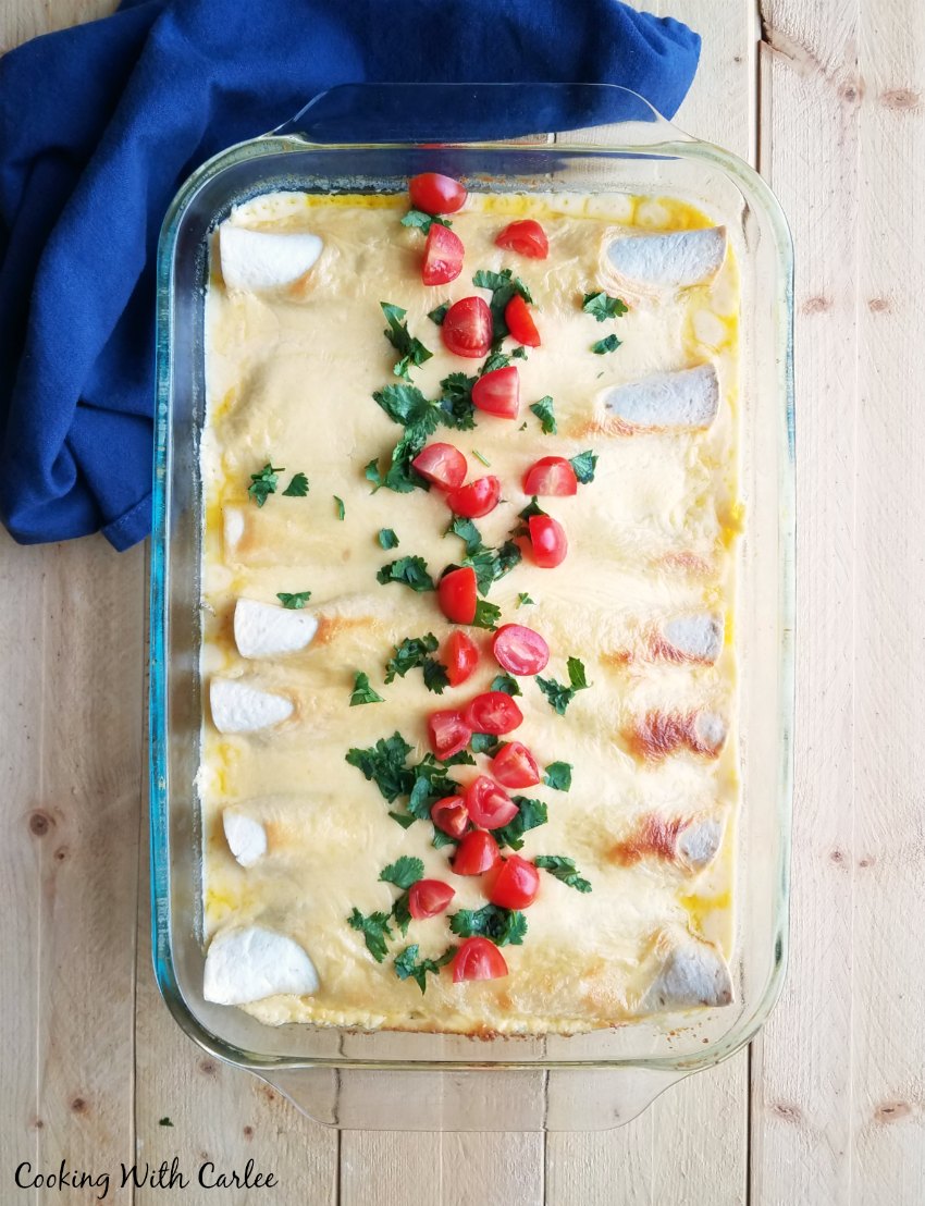 pan of enchiladas with creamy sour cream cheese sauce topped with tomatoes and cilantro.