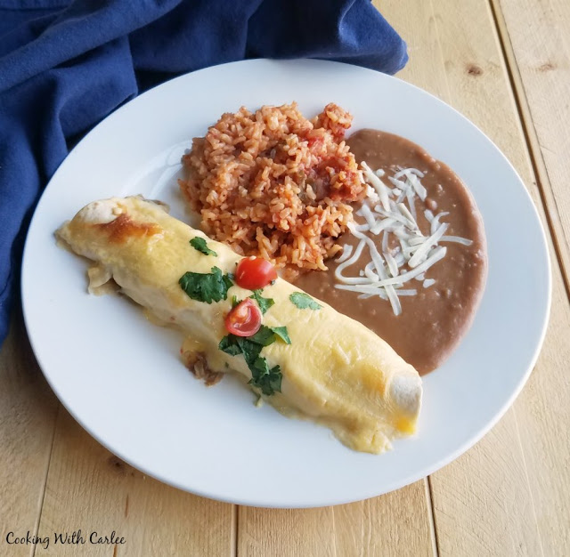 plate of pulled pork enchilada with cream sauce, refried beans and rice
