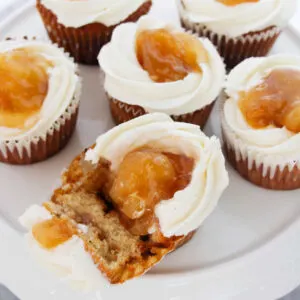 Platter of apple pie filled cupcakes with one broken open showing spiced apple filling.