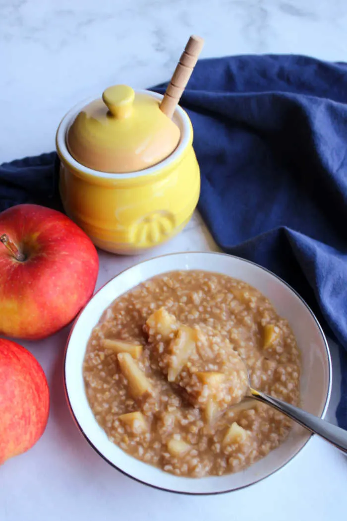 Steel cut oats with lots of apple and cinnamon next to honey jar and apples. 
