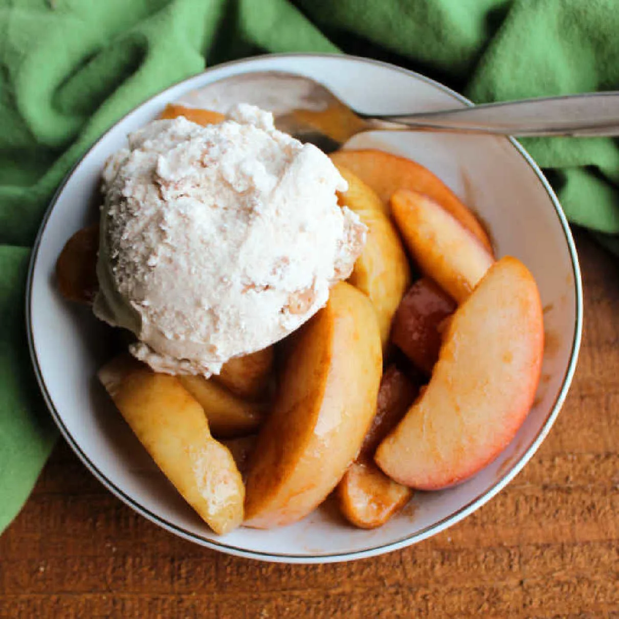 Small bowl of crockpot cinnamon apples served with a scoop of ice cream and a spoon.