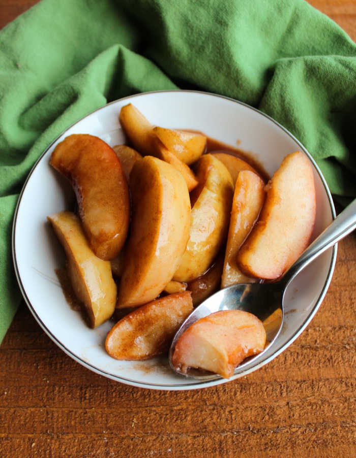 Spoon in bowl of warm cinnamon apples with thick brown sugar sauce.