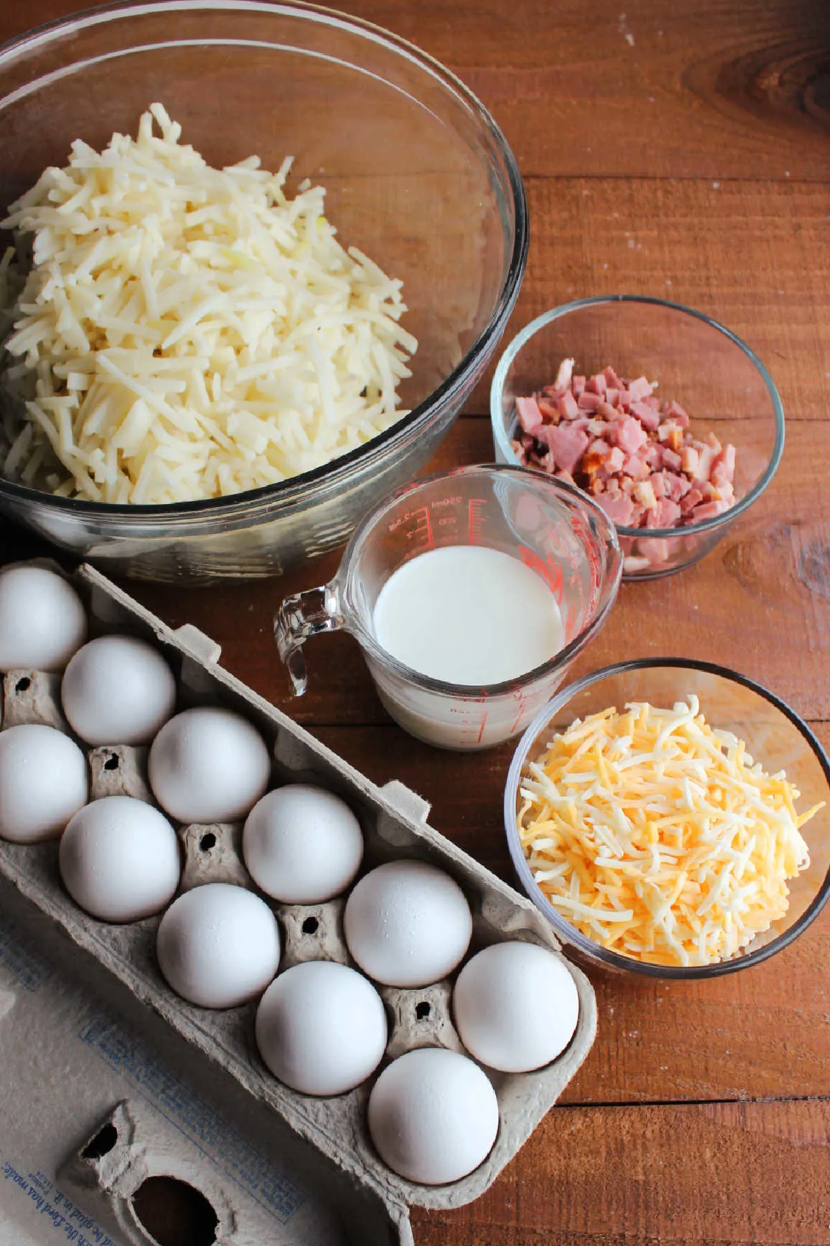 Ingredients including shredded hash browns, eggs, cheese, milk and ham ready to be made into breakfast pizza.