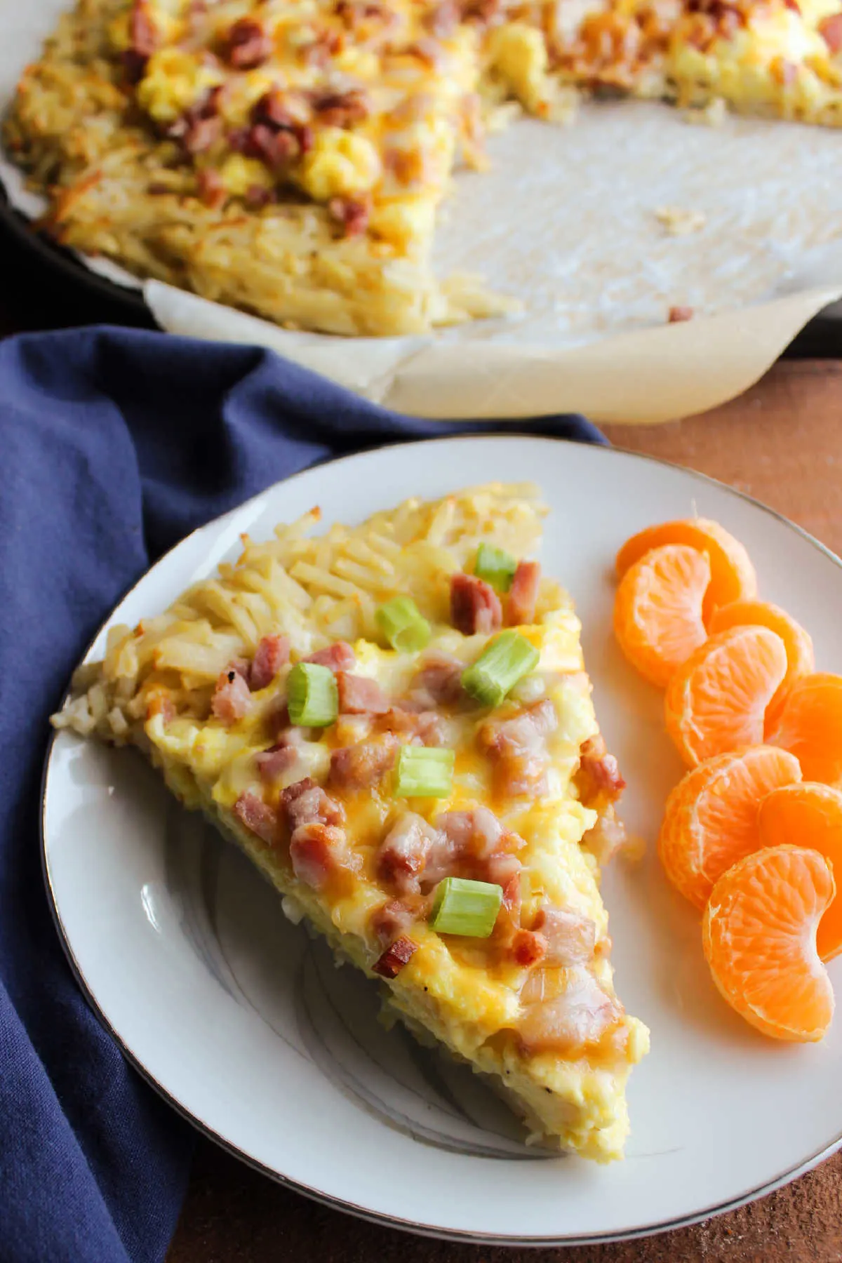 Slice of breakfast pizza topped with green onions served with slices of mandarin orange. 