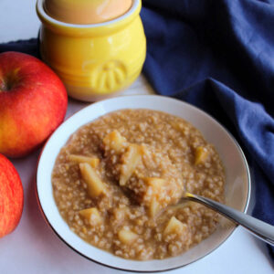 close bowl of steel cut oats with apple chunks next to honey jar and apples