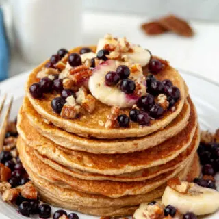 close stack of golden pancakes topped with blueberries, bananas and pecans.