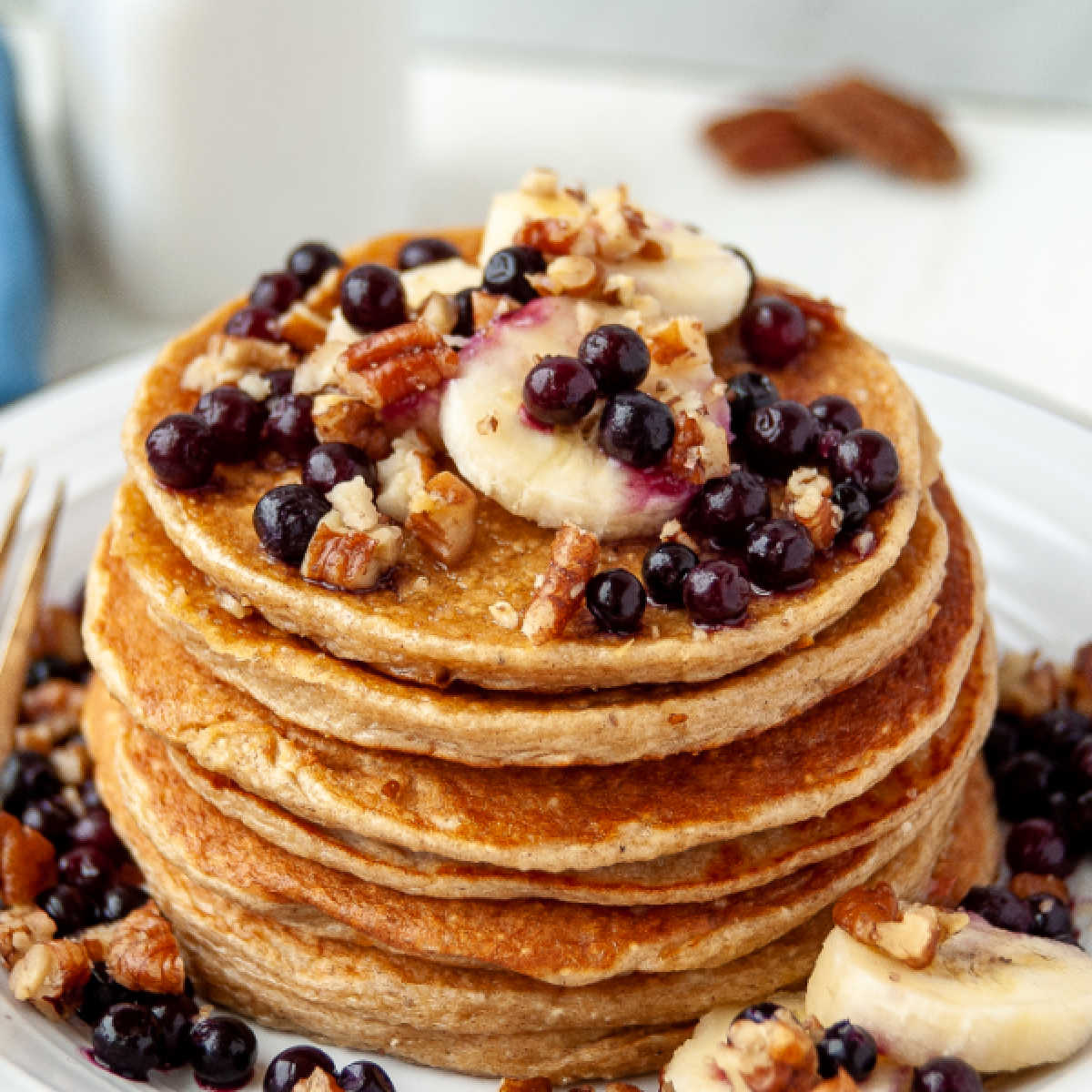 close stack of golden pancakes topped with blueberries, bananas and pecans