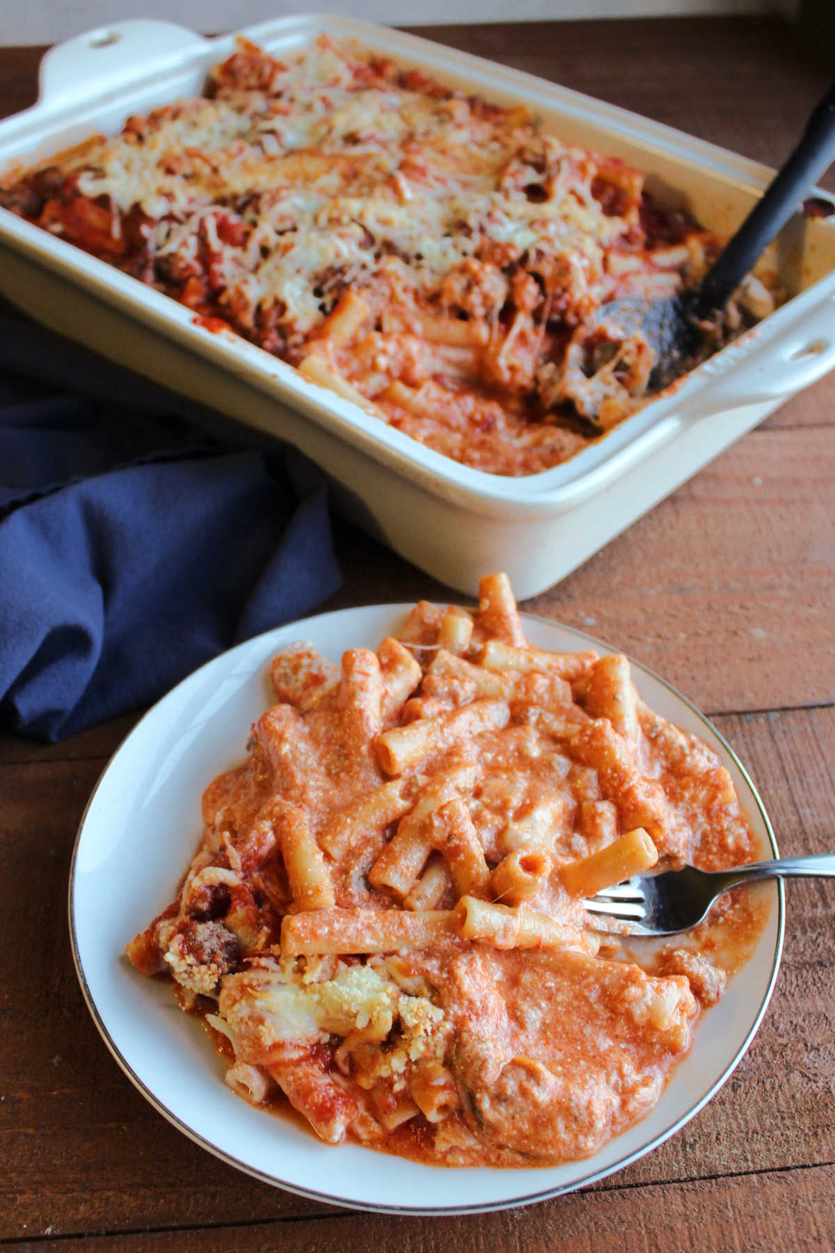 Helping of creamy baked ziti on plate with fork, ready to eat. 