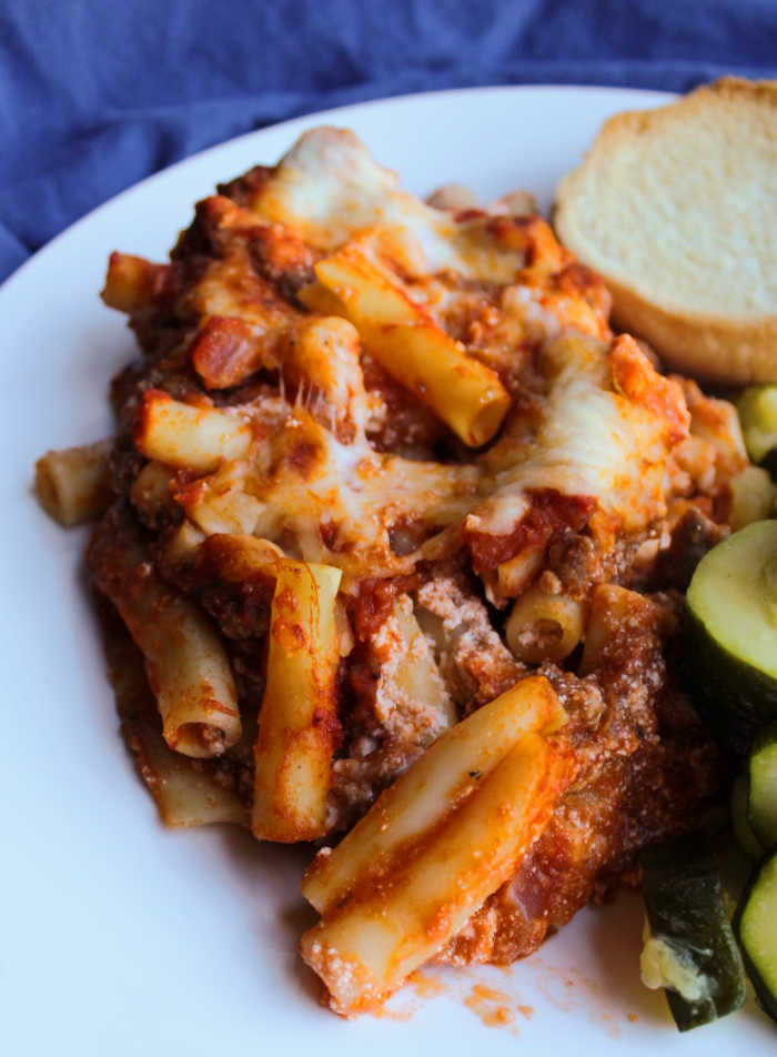 close up of baked ziti on dinner plate with garlic bread and zucchini