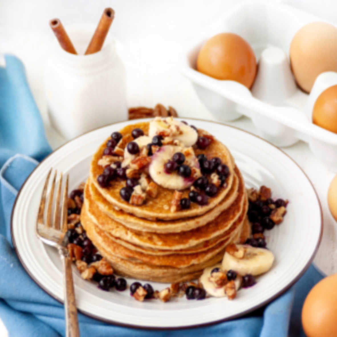stack of pancakes topped with bananas, blueberries and pecans.