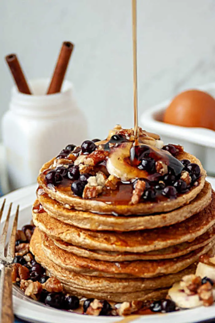 pouring syrup over stack of pancakes with fruit on top