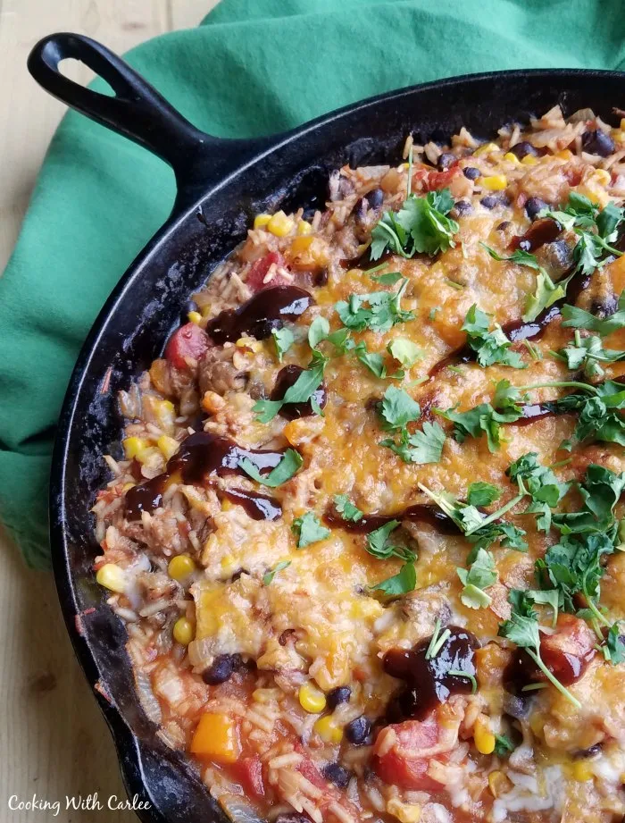 cast iron skillet filled with bbq pulled pork rice topped with melted cheese and chopped herbs. 