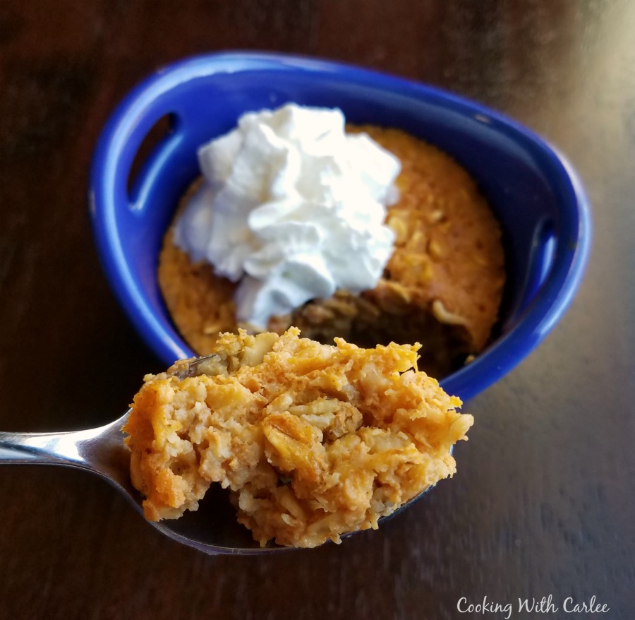 Bite of maple pumpkin baked oats on spoon with ramekin of oats topped with whipped cream in the background.