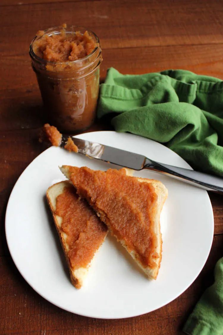 jar of apple butter with knife and apple butter coated toast.