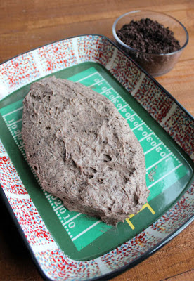 oreo cheese ball mixture shaped like a football with bowl of oreo crumbs nearby for coating the outside