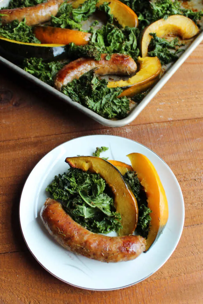 plate with sausage, kale and squash on it with sheet pan in background
