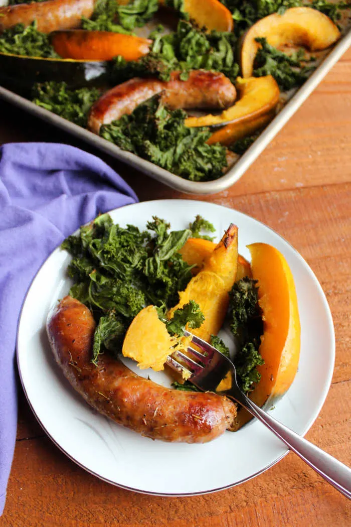 bite of tender acorn squash on fork with plate of kale and sausage