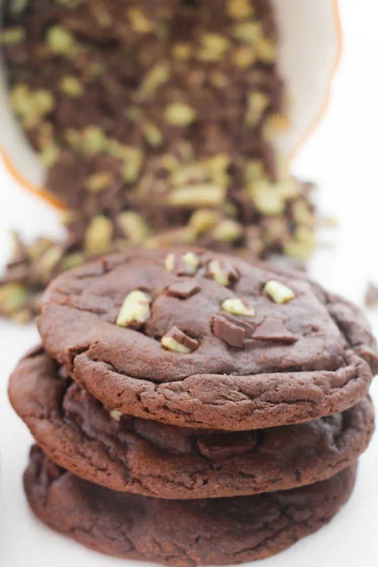 stack of peppermint stuffed chocolate cookies with mint chocolate baking chips in background.