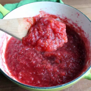 wooden spoon filled with red cranberry applesauce held over pot of sauce.