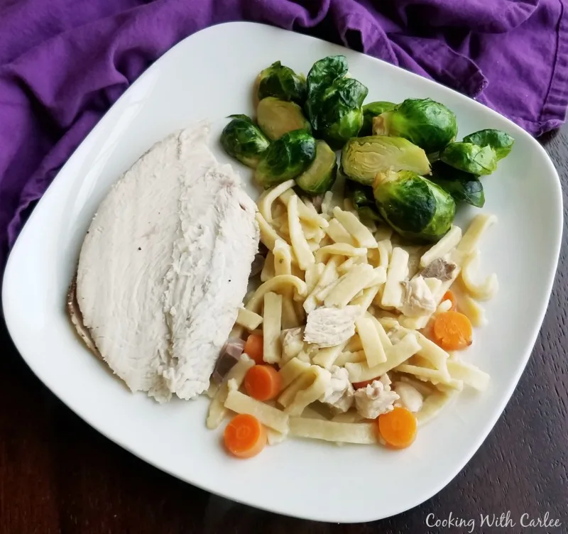 Dinner plate with roasted brussels sprouts, sliced turkey breast, and homemade chicken and egg noodles with carrots.