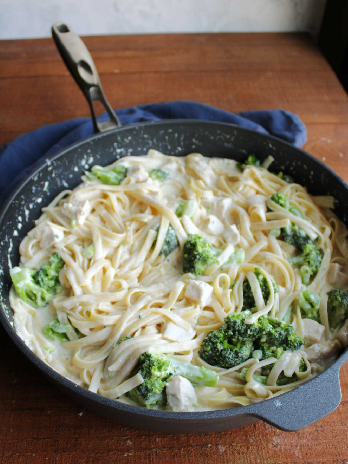 Pan of fettuccine alfredo with broccoli florets and chunks of chicken stirred in, ready to eat.