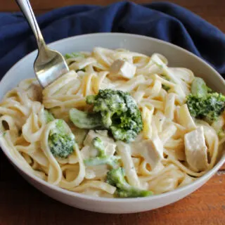 Bowl of fettuccine alfredo with broccoli florets and chunks of chicken with fork wrapped in pasta coated in thick, creamy alfredo sauce.