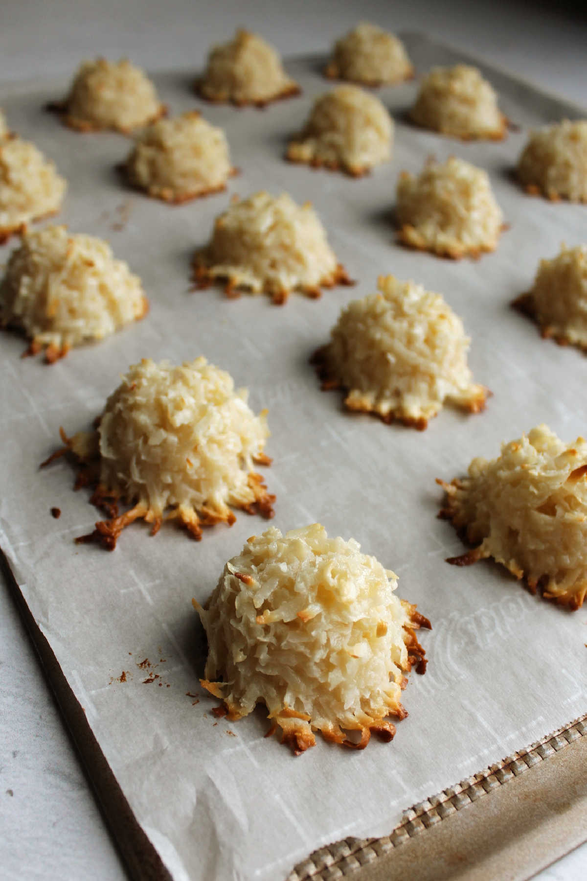 Golden brown coconut macaroons on parchment lined cookie tray fresh from the oven.