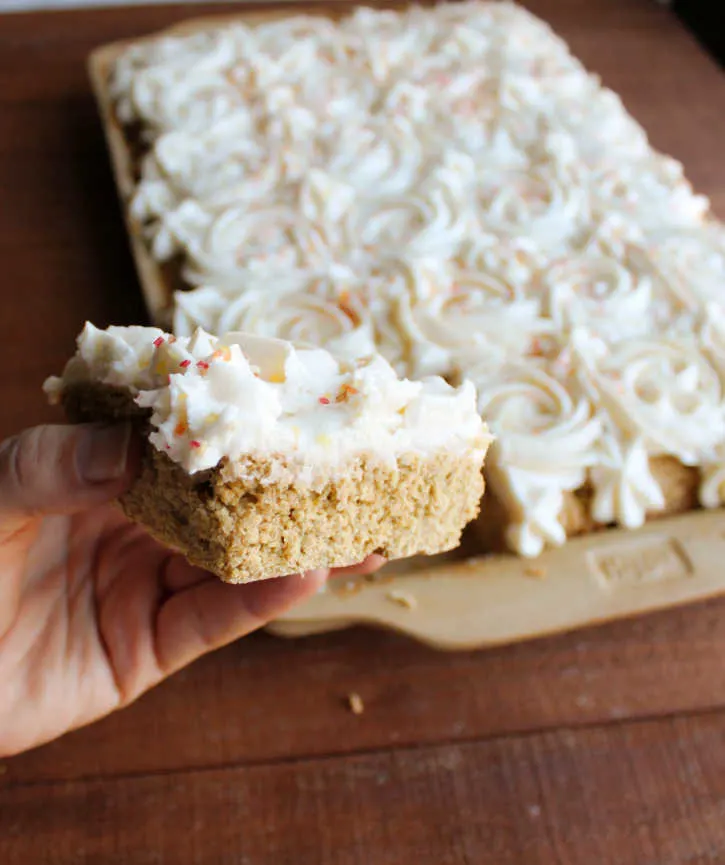 hand holding square of pumpkin cookie bar with frosting rosettes on top.