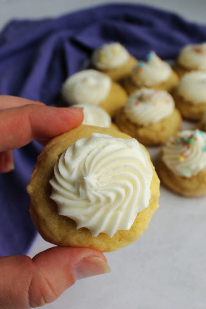 Hand holding freshly baked sour cream sugar cookie topped with frosting.