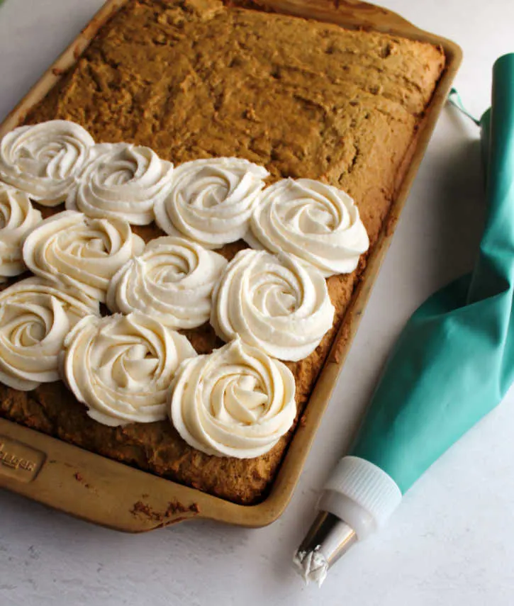 tray of pumpkin spice bars with piping bag of buttercream putting rosettes on top.