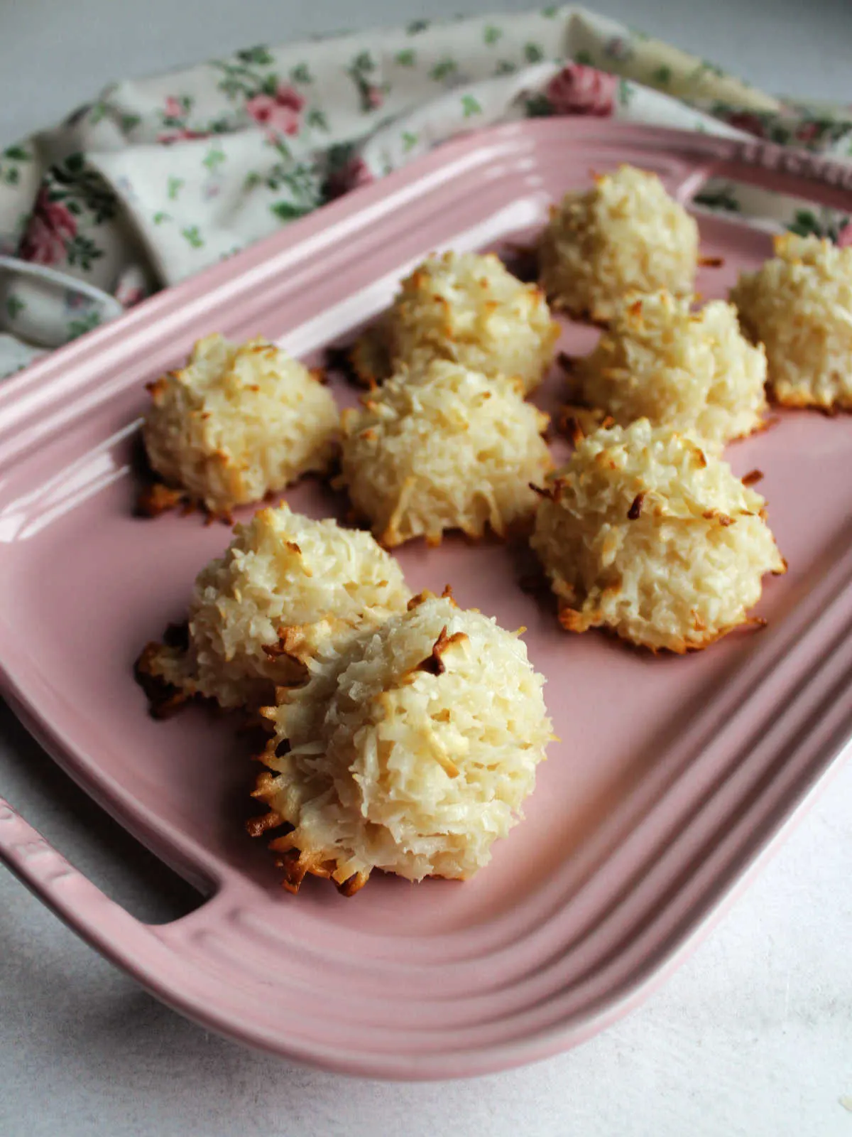Pink platter of coconut macaroons showing golden brown edges and puffy white coconut cookies. 