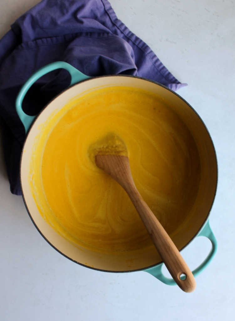dutch oven of creamy pumpkin soup with wooden spoon.