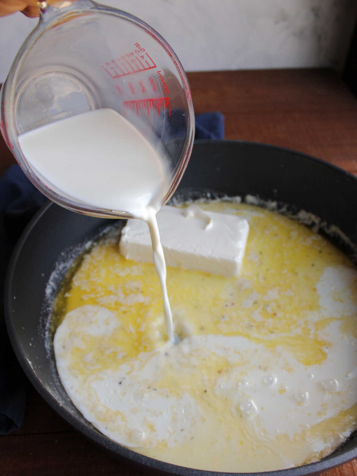 Pouring milk into pan that has melted butter and a brick of cream cheese inside.